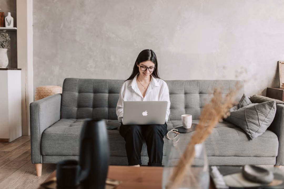 Eine Frau sitzt mit dem Laptop auf dem Sofa und schreibt eine Anfrage